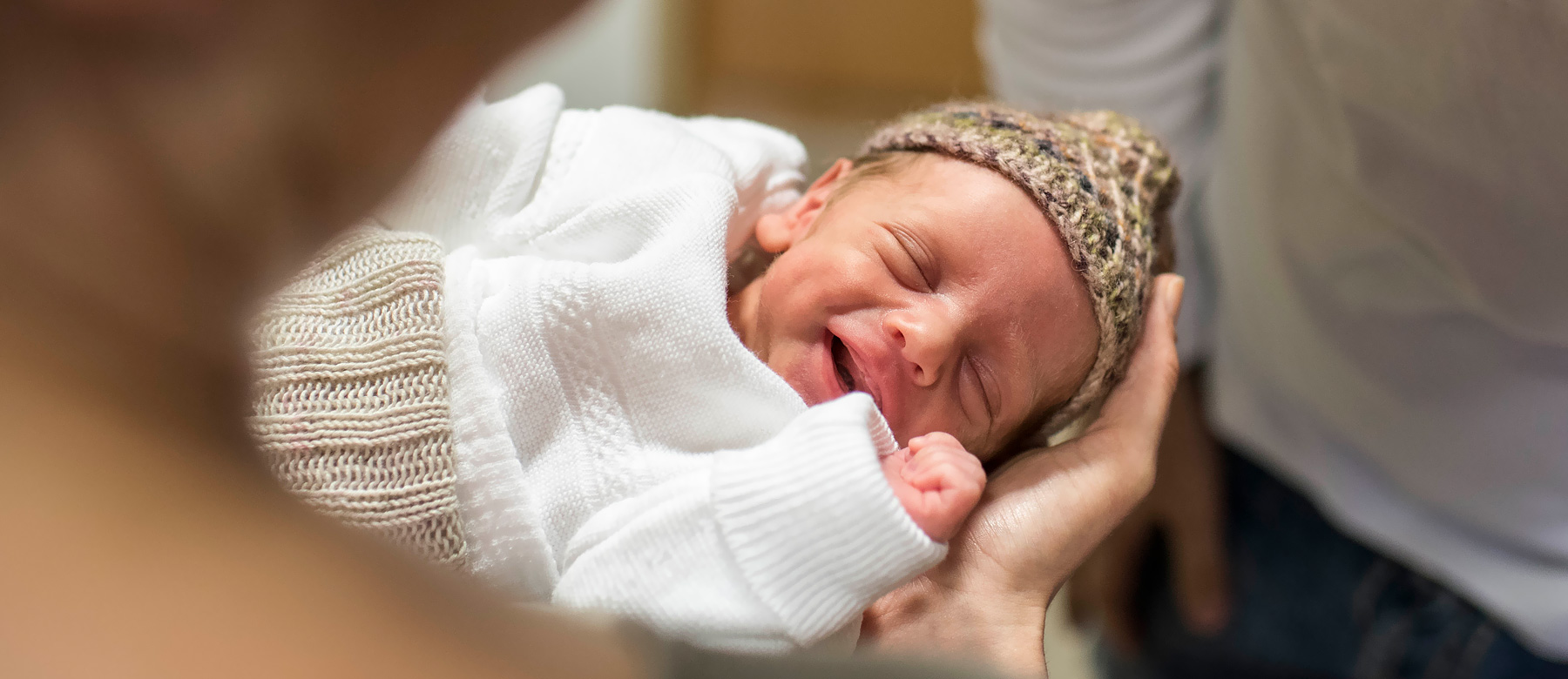 Schlafendes Neugeborenes liegt in den Händen seiner Mutter und lächelt.