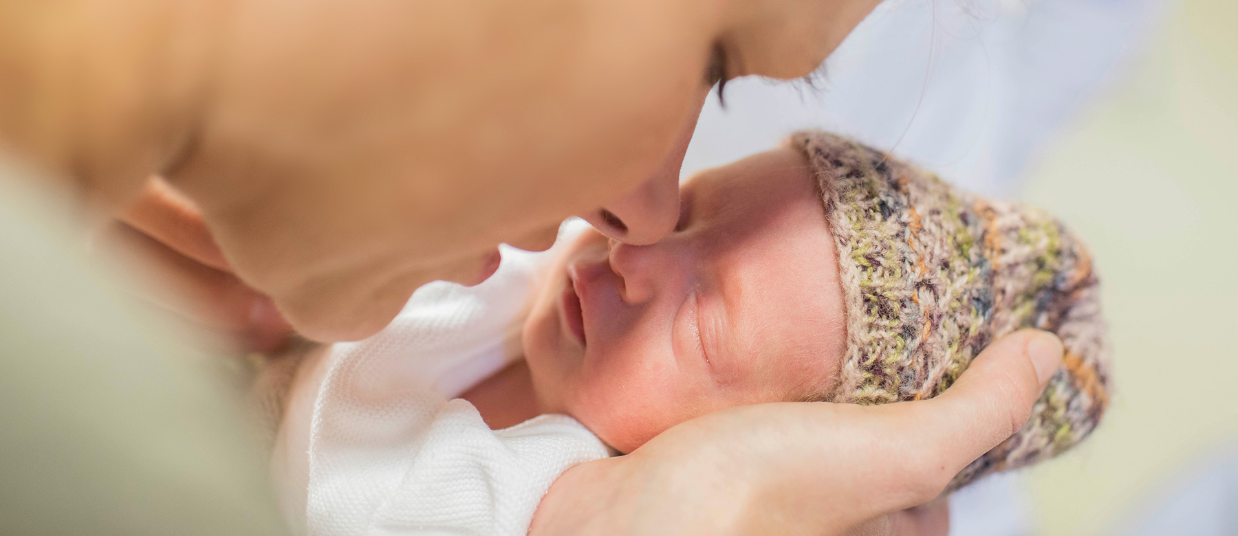 Mutter hält ihr Neugeborenes in den Händen und berührt mit ihrer Nase die Nase des Kindes.