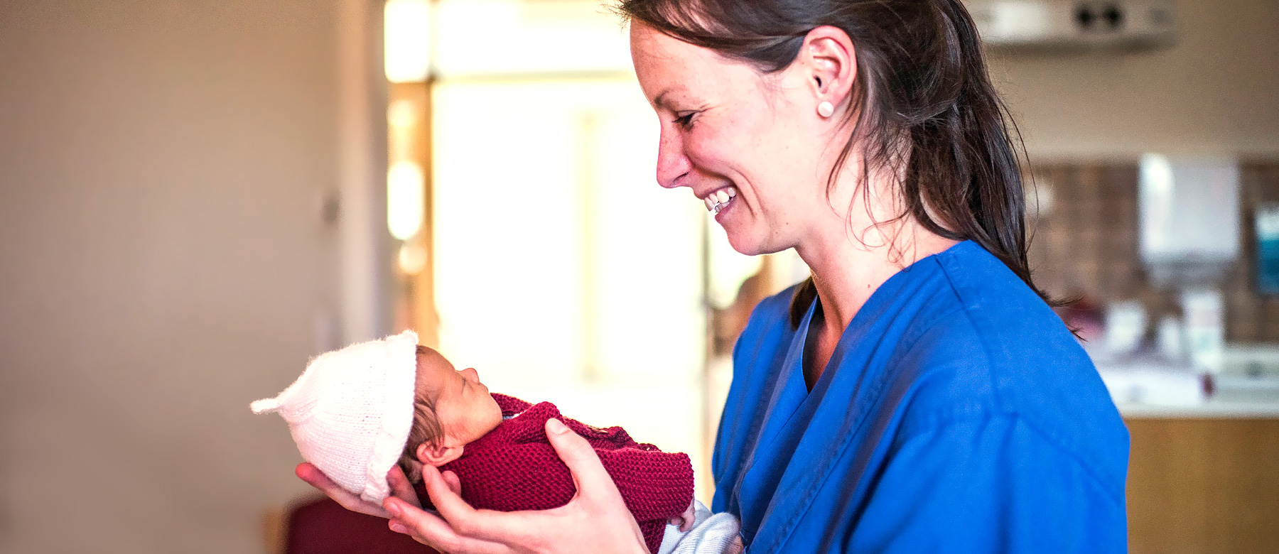Kinderkrankenpflegerin in der Neonatologie hält ein frühgeborenes Baby in den Händen und lächelt.
