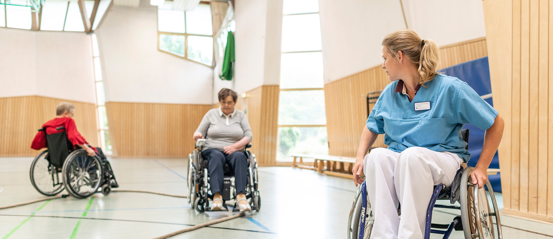 Physiotherapeutin übt das Rollstuhlfahren mit zwei Patientinnen.