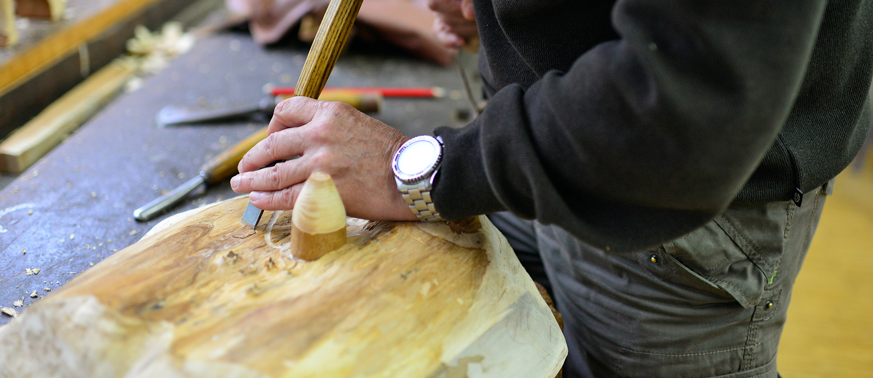 Patient bearbeitet mit einem Stecheisen eine Holzskulptur.