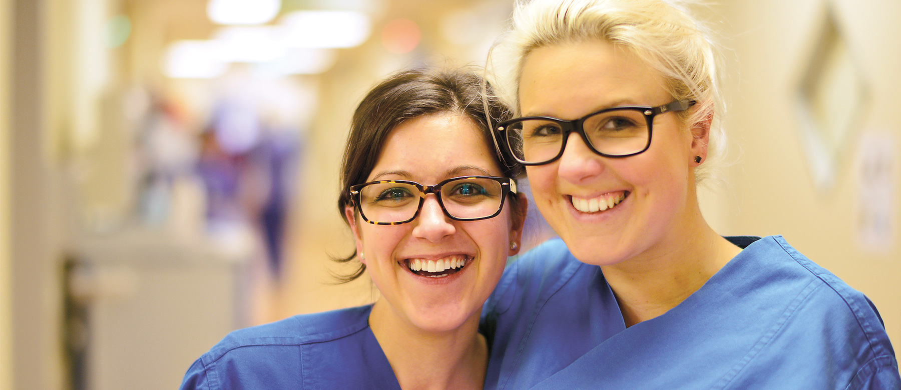 Zwei Intensivkrankenschwestern umarmen sich und lachen in die Kamera.