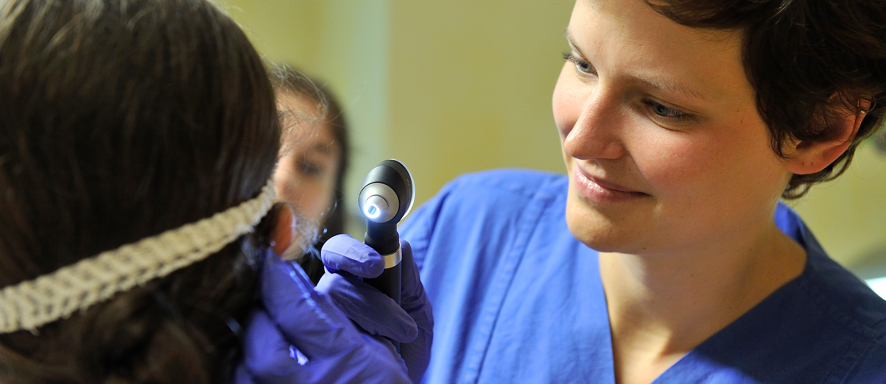 Ärztin untersucht mit einem Otoskop das Ohr einer Patientin.
